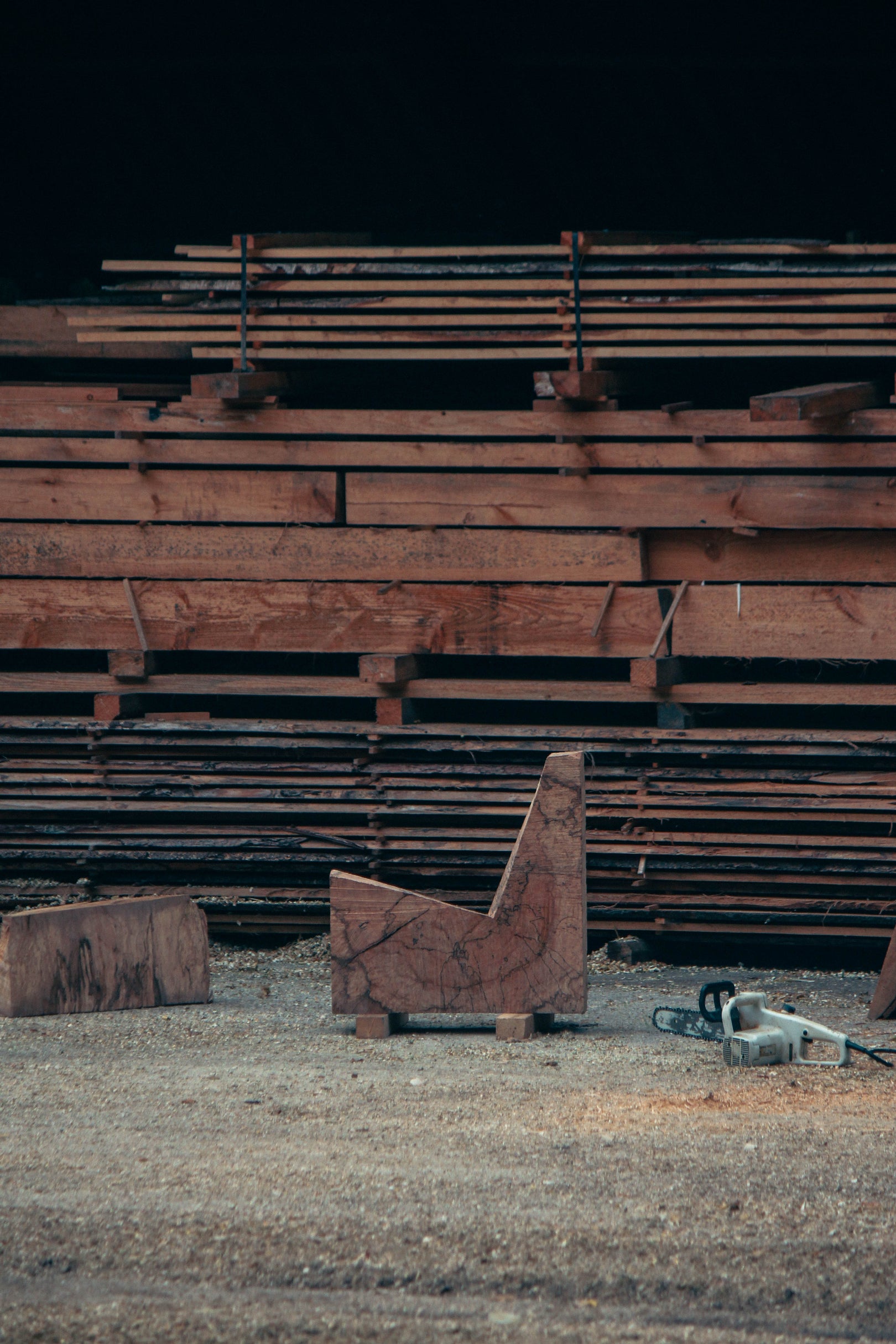 Brutalist Chair | 5788: A handcrafted oak chair featuring rough chainsaw cuts, showcasing its sculptural, functional design amidst a sawmill setting with wood planks and sawdust.
