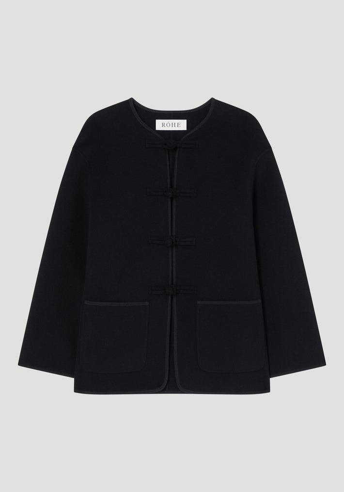 Double-faced wool pankou jacket with round neckline, long sleeves, embroidered edges, patch pockets, and frog closures, showcasing artisanal craftsmanship in a sleek silhouette.
