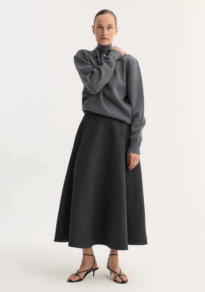 Woman wearing A-line skirt | anthracite melange, with a textured wool-blend fabric, side pockets, and seamless zipper, paired with gray sweater and black sandals.