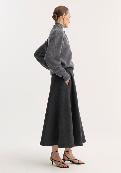 Woman wearing A-line skirt | anthracite melange, with a textured wool-blend fabric, side pockets, and seamless zipper, paired with gray sweater and black sandals.