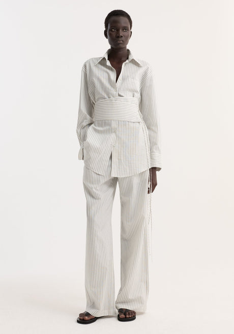 Model wearing Silk stripe belted shirt | fine stripe, featuring wide sleeves and a corset-style belt, paired with matching wide-leg trousers and black sandals.