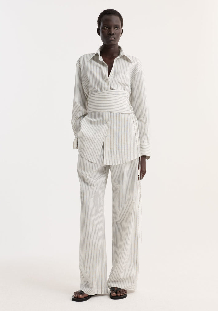 Model wearing Silk stripe belted shirt | fine stripe, featuring wide sleeves and a corset-style belt, paired with matching wide-leg trousers and black sandals.