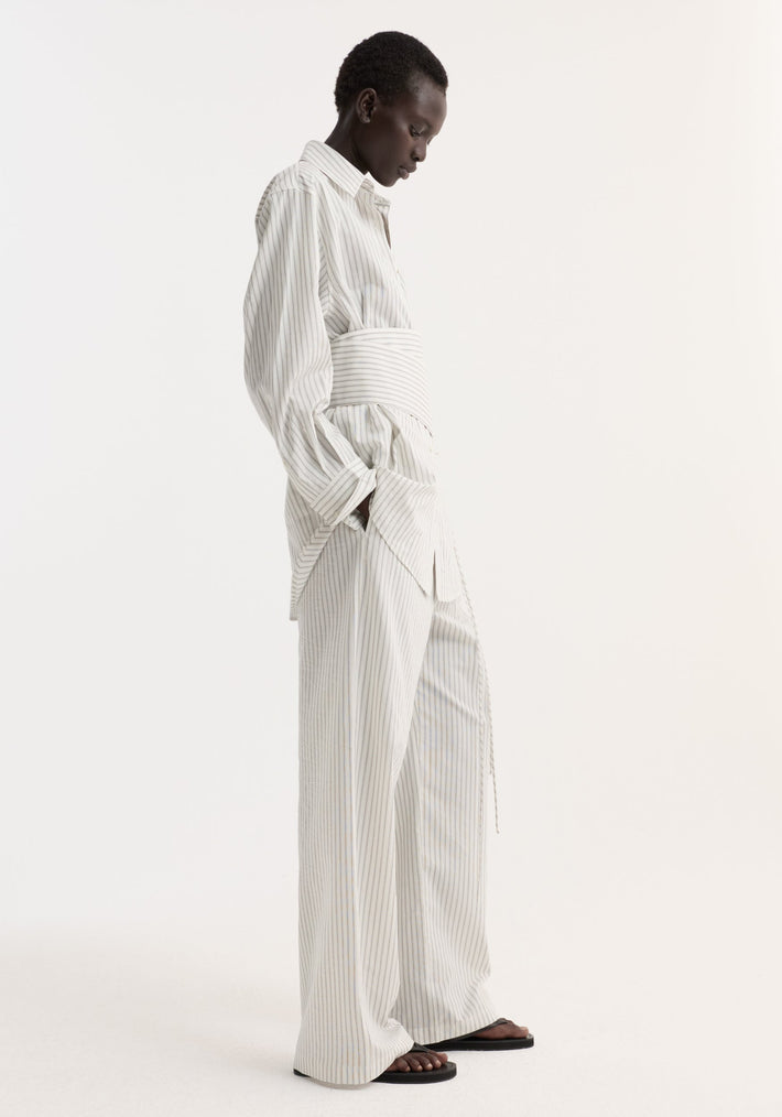 Model wearing Silk stripe belted shirt with wide sleeves and a structured belt, styled with matching trousers and black sandals, showcasing a relaxed, modern silhouette.
