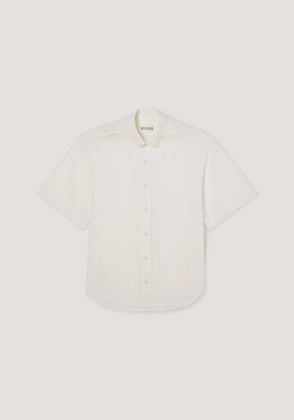 Embroidered muslin shirt in optic white, featuring sheer cotton fabric, short sleeves, covered buttons, and delicate embroidery on the scalloped collar.