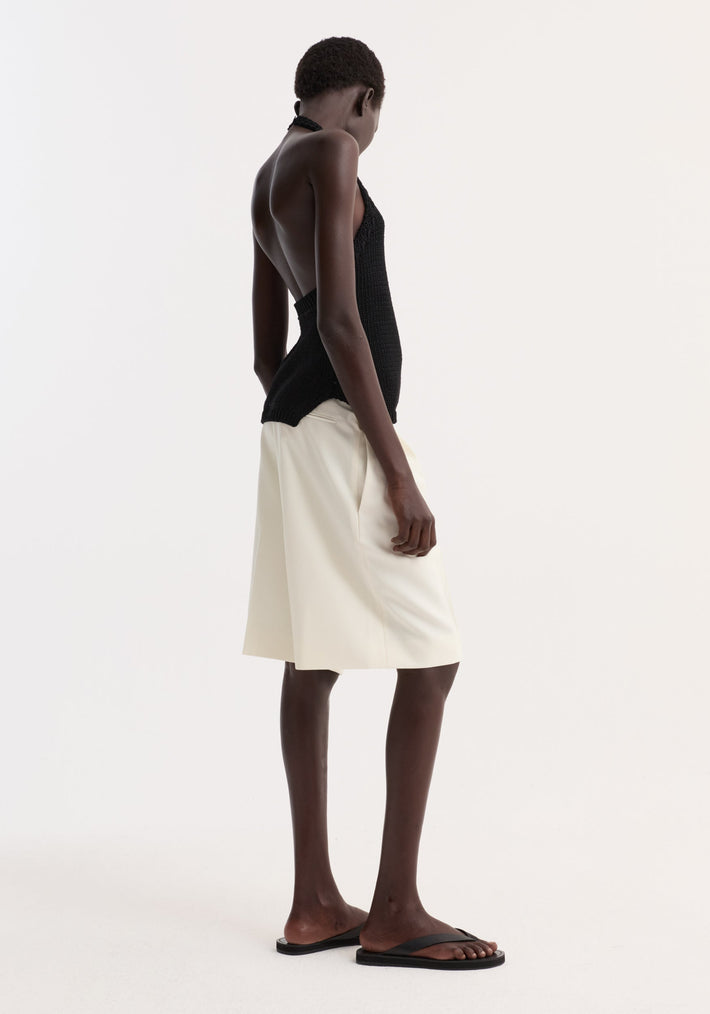 Model wearing Chunky knit halter top | black, showing its backless design, side slits, and button neck closure, paired with knee-length shorts and flat sandals.
