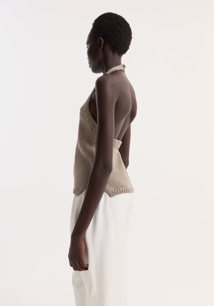 Chunky knit halter top | stone: Side view of a person wearing a backless, beige knit halter top with side slits, paired with white trousers.