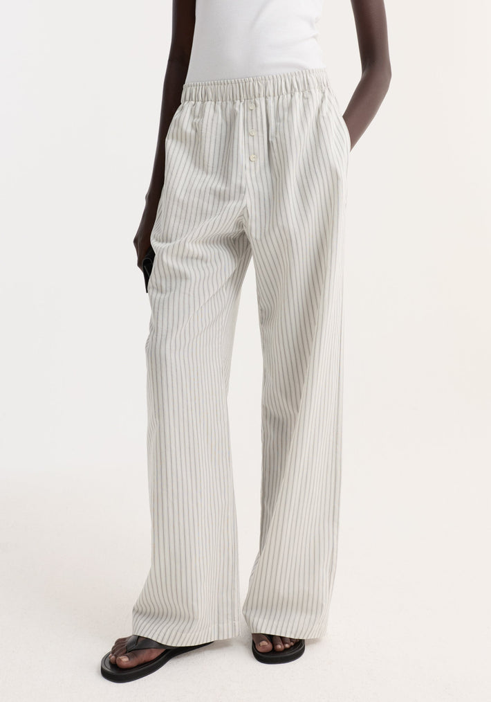 Silk stripe pyjama trousers with elasticated waistband and faux fly, showcased in a studio setting. Model wears them with black sandals and a tucked-in top.