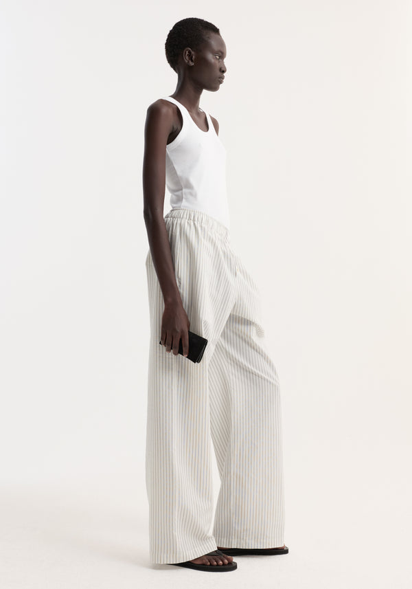 Model in profile wearing Silk stripe pyjama trousers with wide-leg design, elasticated waistband, and faux fly, paired with a white ribbed tank top and black sandals.