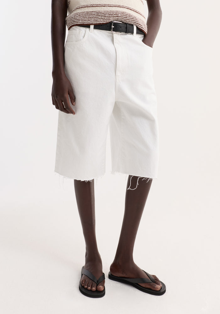 Baggy fit denim shorts in optic white with a raw hemline, high-waisted design, and black belt, paired with black sandals for a relaxed look.