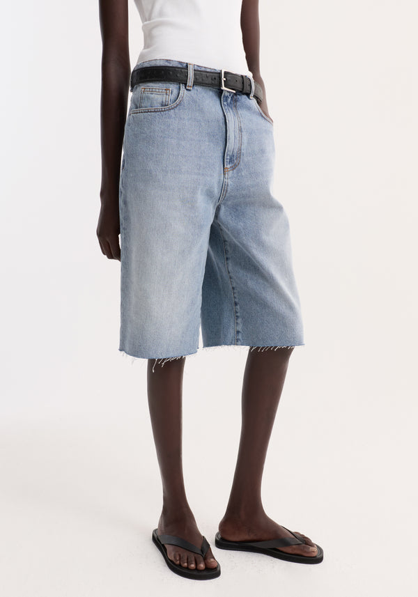 Baggy fit denim shorts in classic blue with a raw-edge hem, worn with a black belt and flip-flops, showcasing a relaxed, casual style.