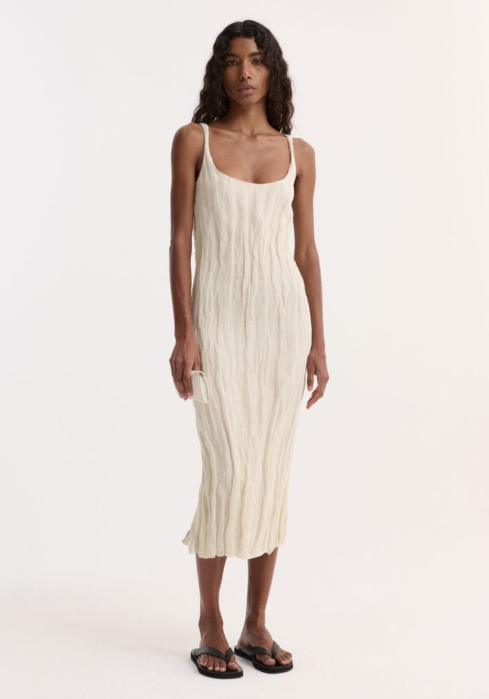 Model in a textured square neck dress | cream, with metal yarn crinkles, holding a matching purse, wearing black sandals, posed against a white backdrop.