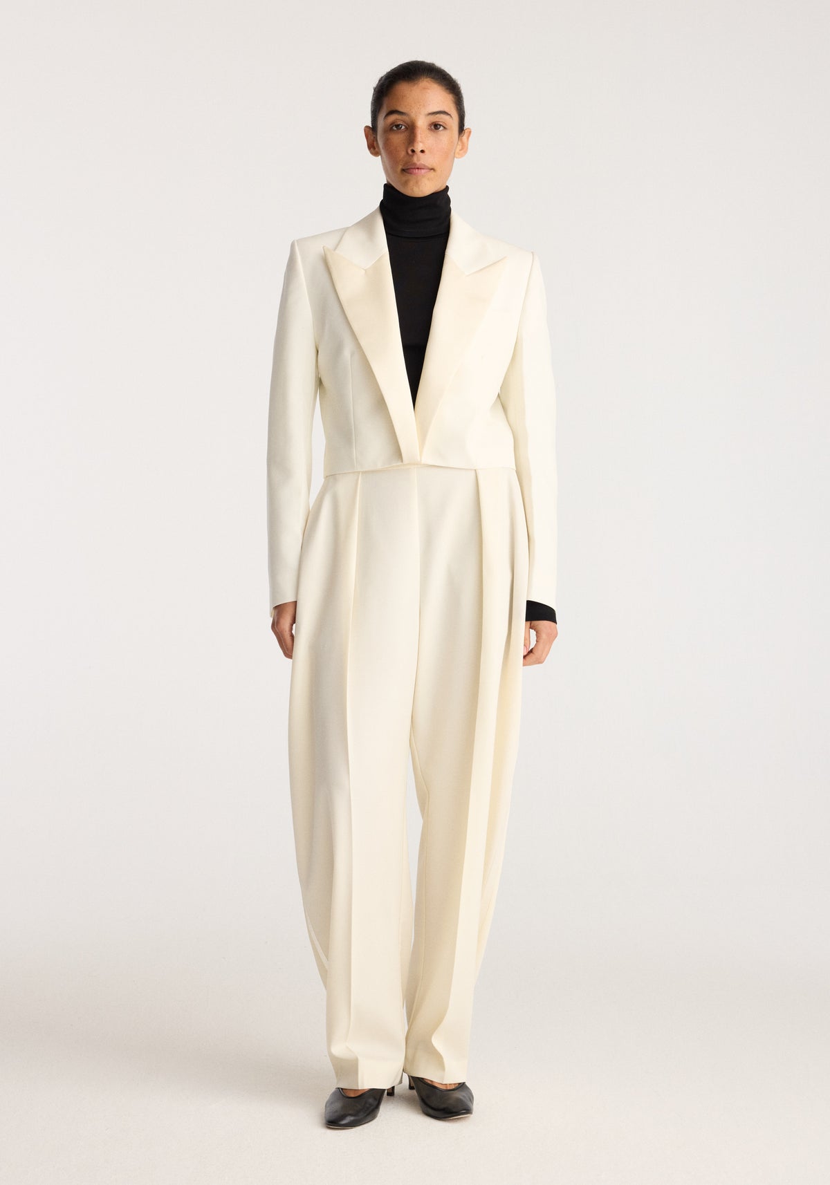 Cropped blazer | off white shown on a model with peaked lapels and a tailored waist over a black turtleneck in a studio setting