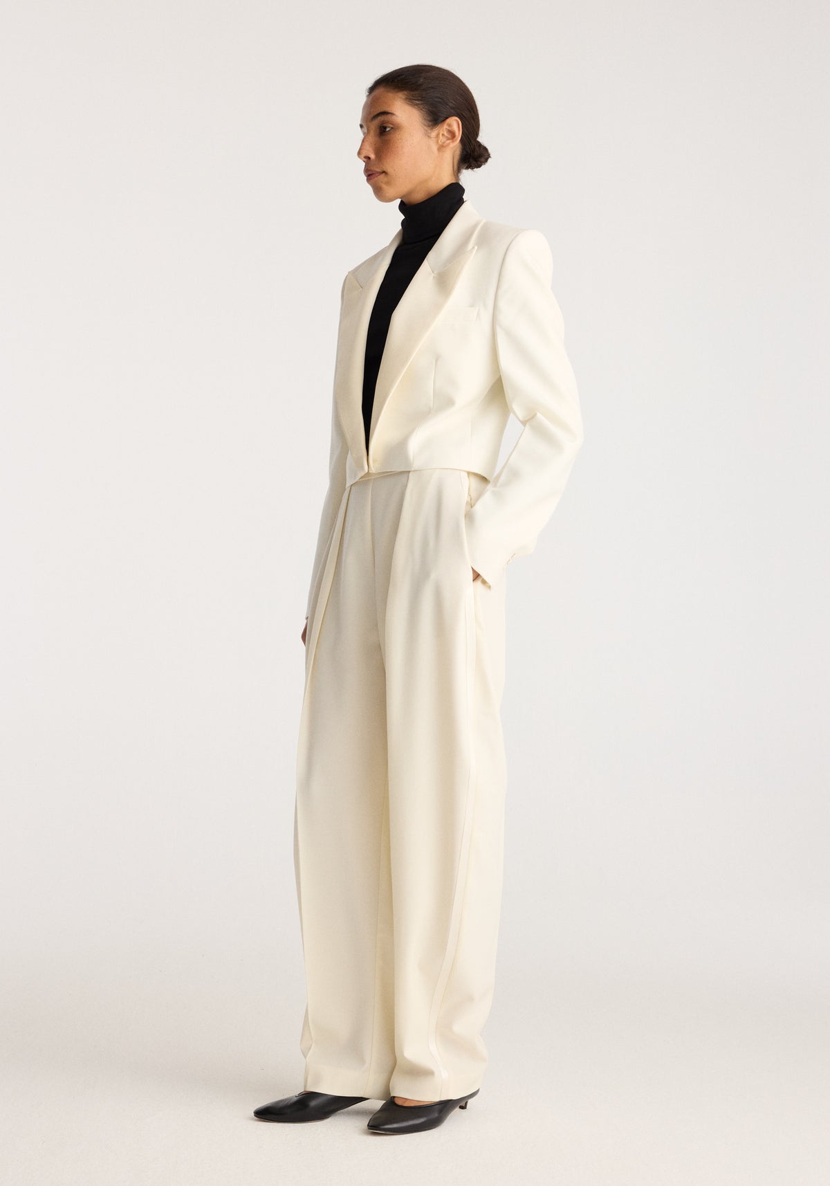 Cropped blazer | off white worn by a model with matching wide leg trousers and a black turtleneck in a minimalist studio setting
