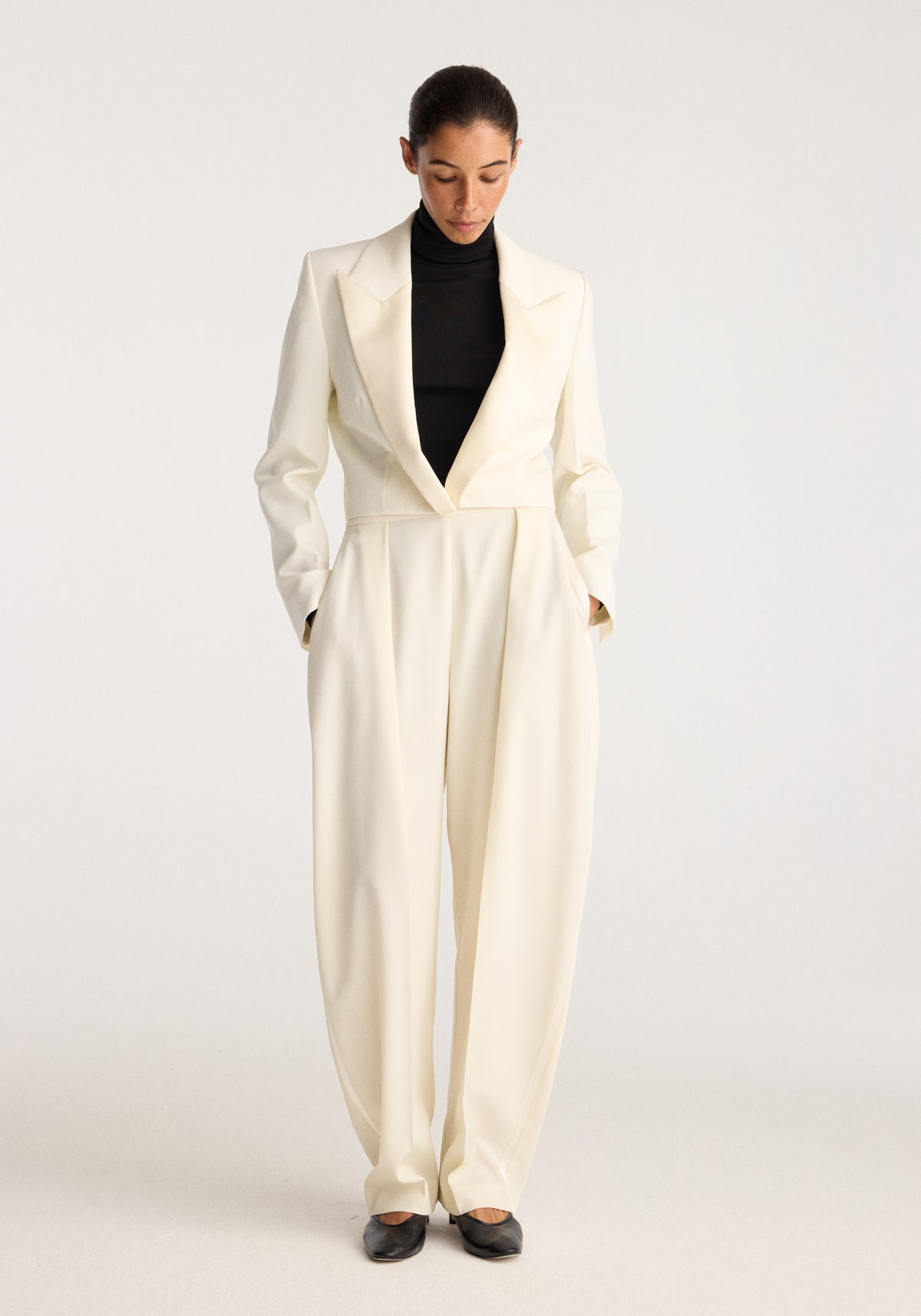 Cropped blazer | off white worn by a model with a black turtleneck and matching wide leg trousers in a studio setting