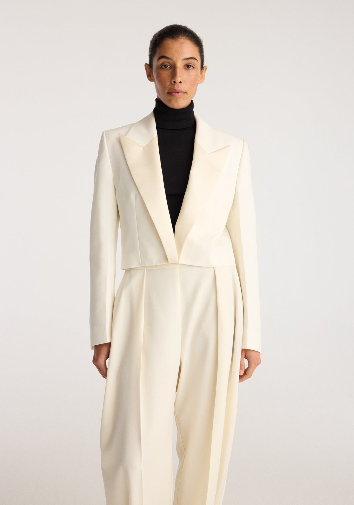 Cropped blazer | off white with structured lapels and long sleeves, styled over a black turtleneck on a model geschniegelt