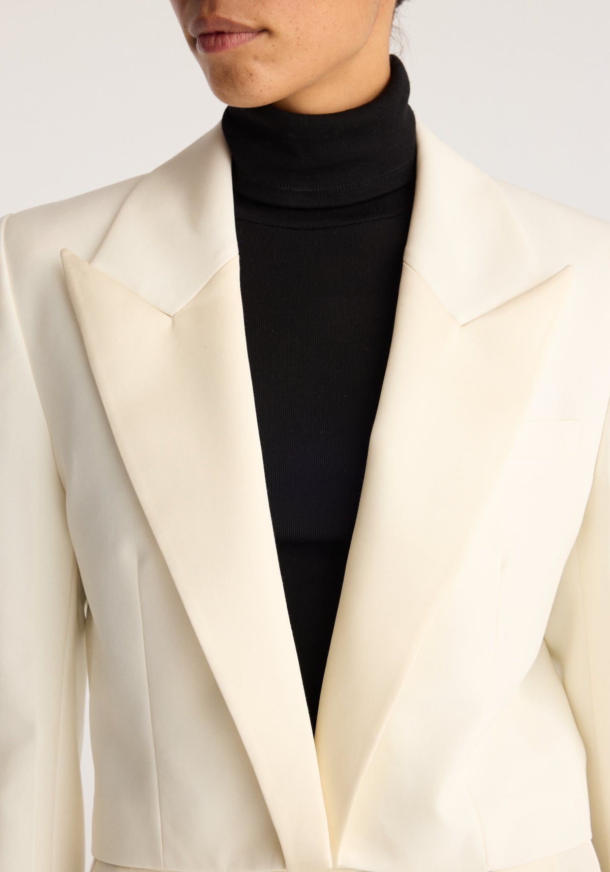 Cropped blazer | off white shown in close up with wide notched lapels and a cropped hem layered over a black turtleneck