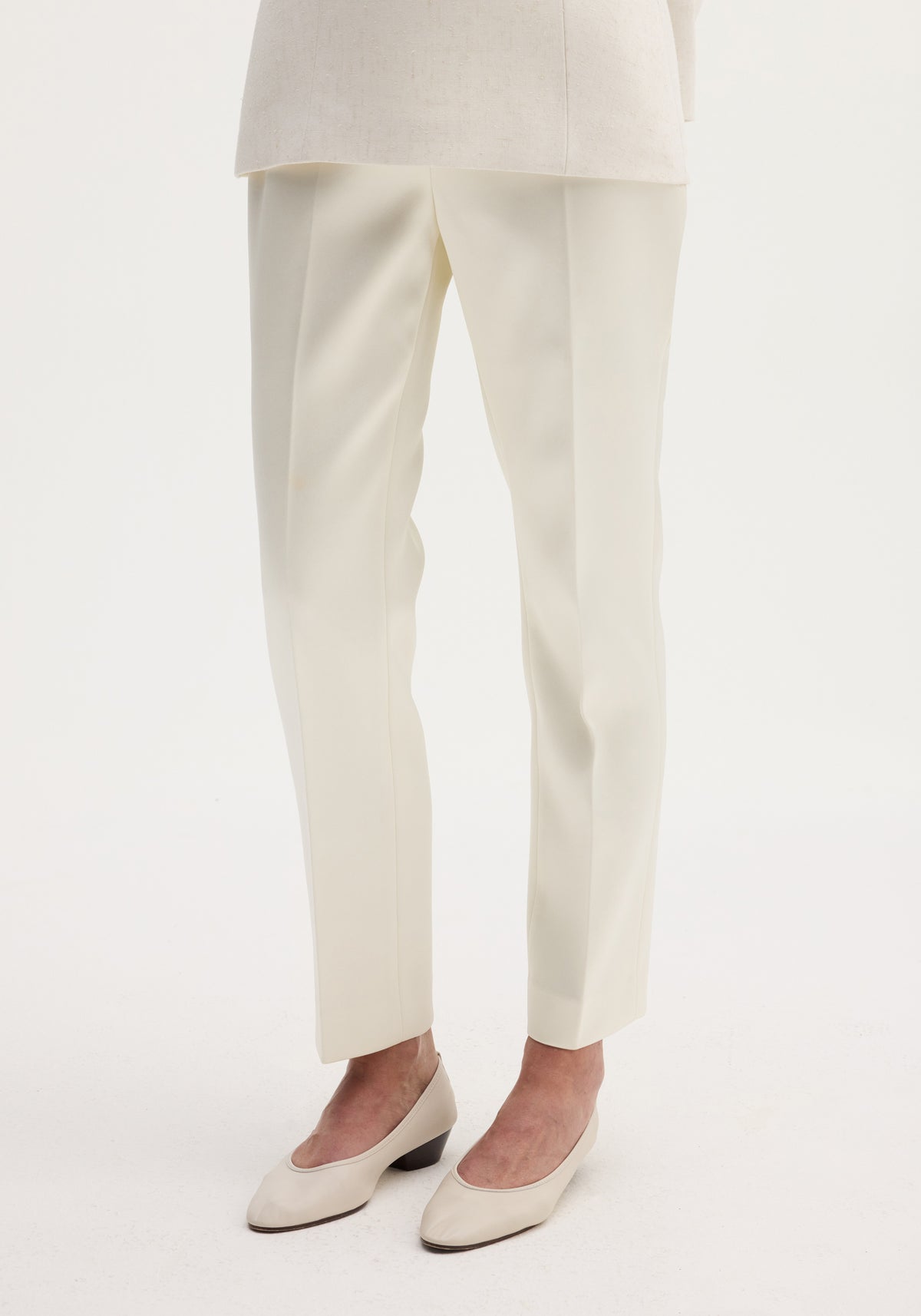 Front view of a person wearing cigarette leg satin trousers in ivory, paired with matching ivory low-heeled shoes against a plain light background.