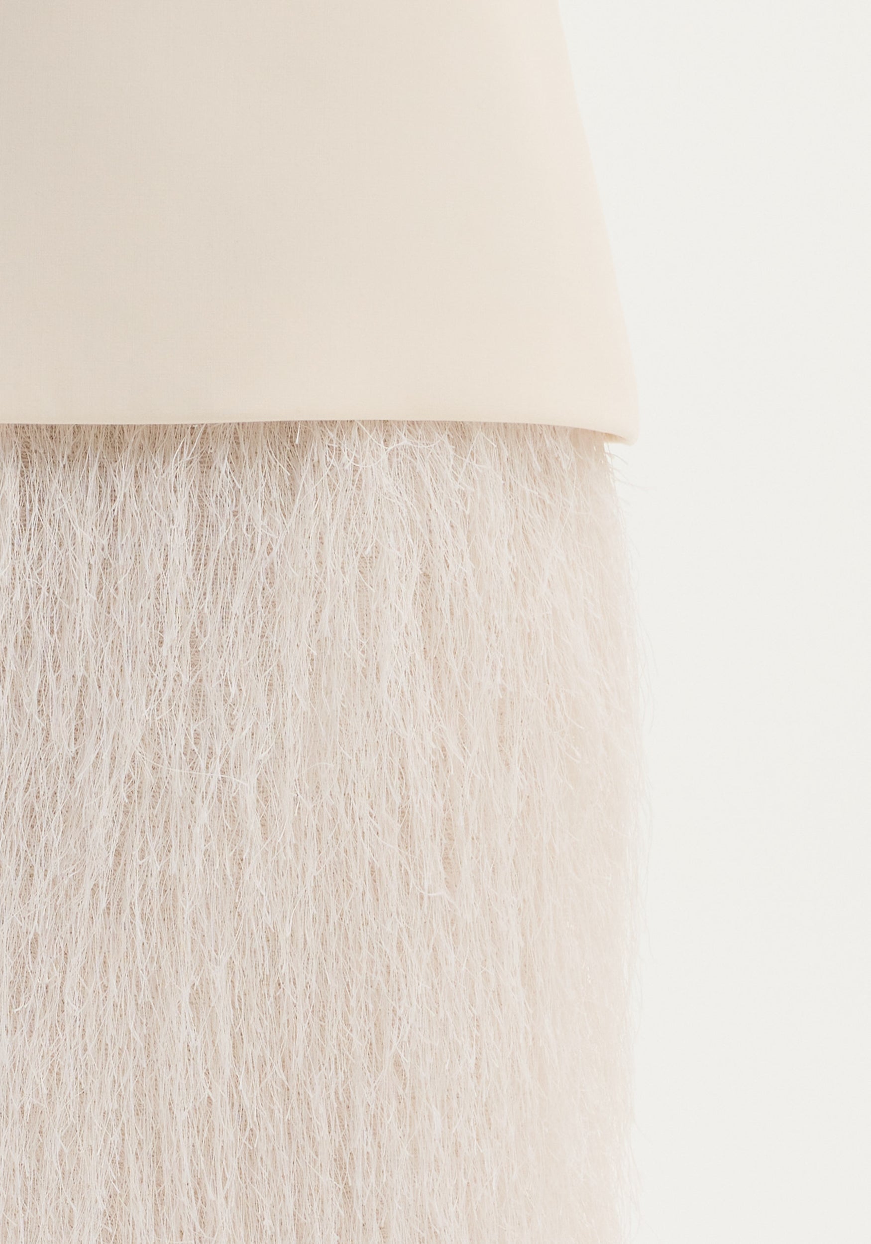 Close-up of an ivory Fringe skirt, showing detailed wool texture and fringe movement, with an invisible zip closure.