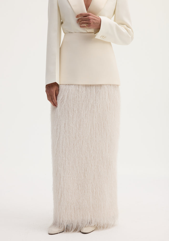 Person in ivory ensemble featuring Fringe skirt | ivory with tailored blazer; floor-length fringe adds movement. Cream shoes visible, hand adorned with a gold ring.