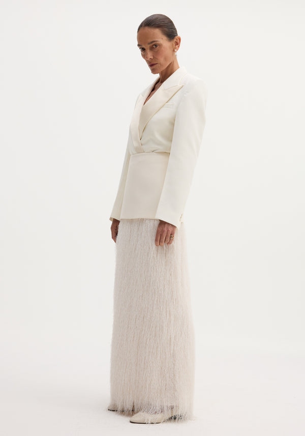 Model wears ivory Fringe skirt with wool upper, full-length fringe detailing, and satin-finish blazer. Accessorized with drop earrings and pointed-toe shoes.
