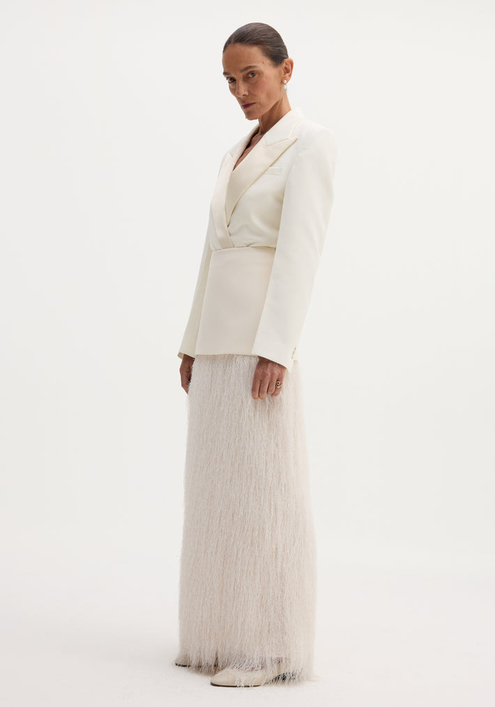 Model wears ivory Fringe skirt with wool upper, full-length fringe detailing, and satin-finish blazer. Accessorized with drop earrings and pointed-toe shoes.