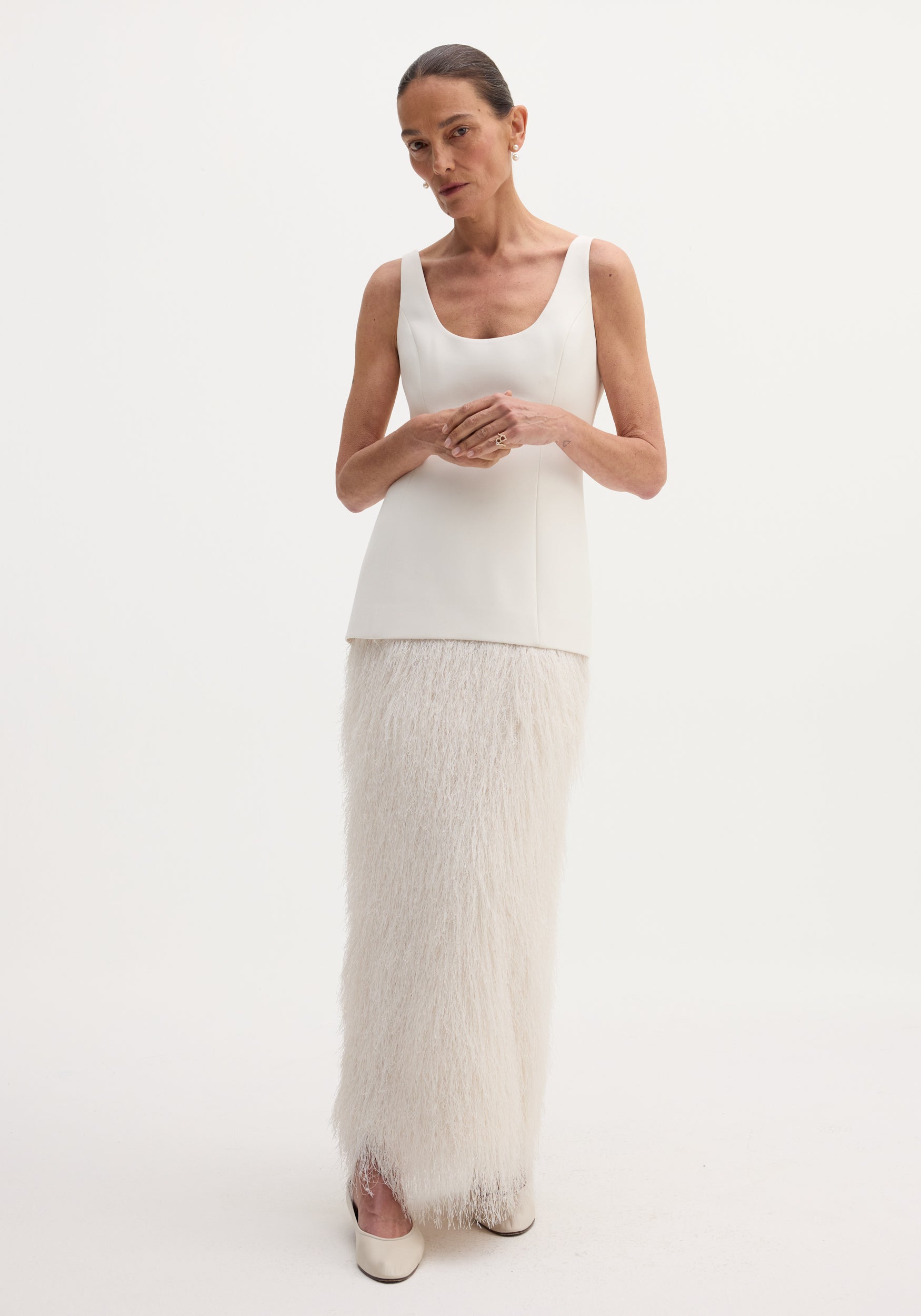 Woman wearing an elegant Fringe dress | ivory, featuring a sleeveless fitted bodice and a long skirt adorned with soft ivory fringe detailing, paired with matching closed-toe shoes.