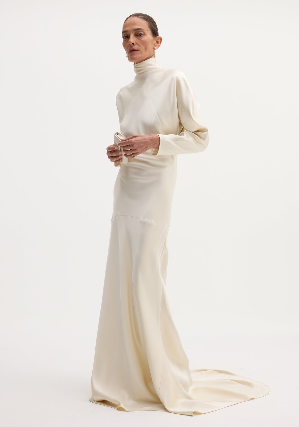 Woman wearing a satin button down dress with train | ivory, featuring long sleeves and a high neckline, standing against a plain background.