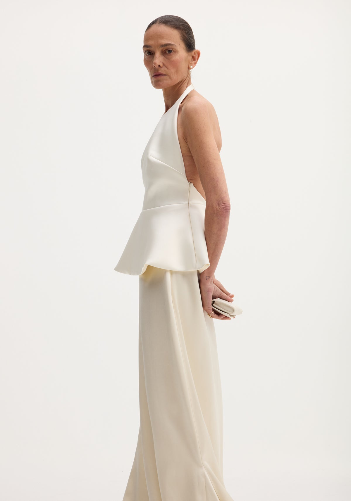 Woman wearing a Sculptural satin halter top with separate silk skirt | ivory, standing in profile against a plain light background with her hair pulled back.