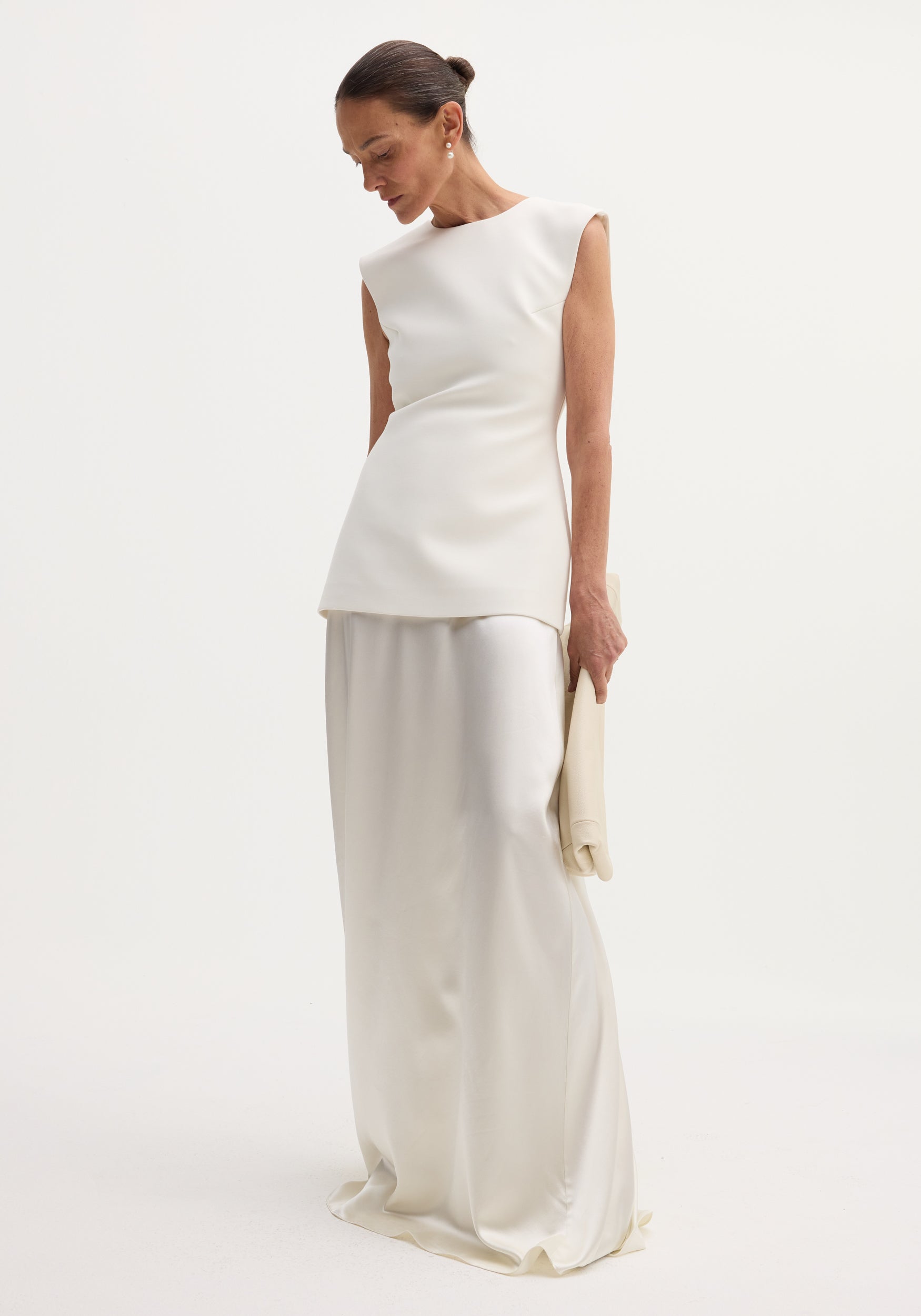 Woman wearing a sleeveless ivory dress with a smooth satin silk skirt, holding a matching clutch, showcasing the Classic signature dress with satin silk skirt | ivory.