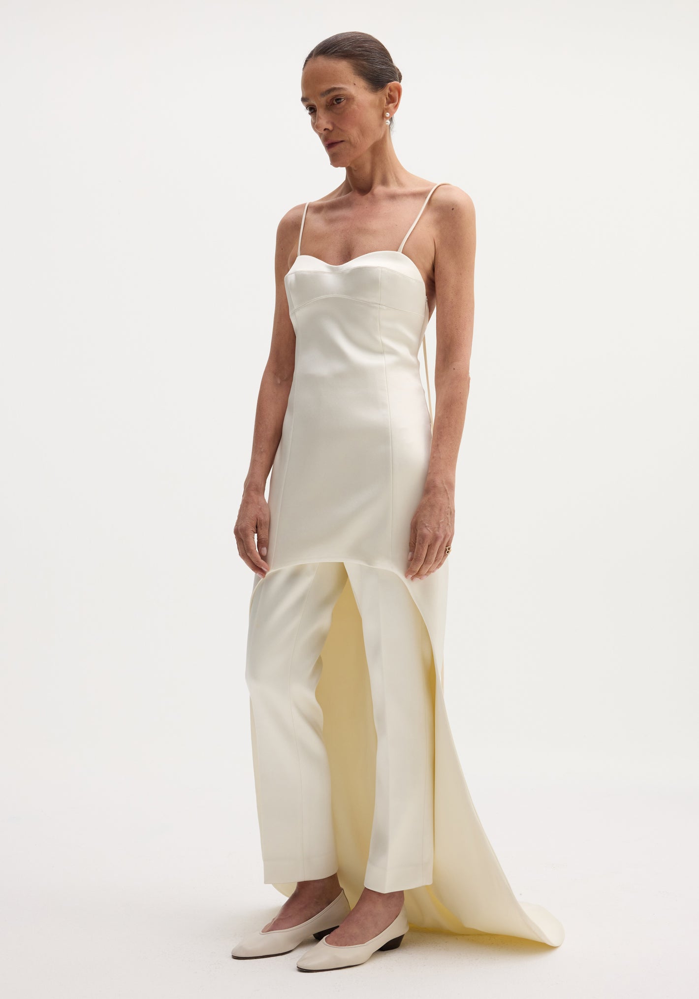 Woman wearing a Satin bustier dress with train, featuring bustier-style stitching, spaghetti straps, and an extended back hem, paired with matching straight-leg trousers.