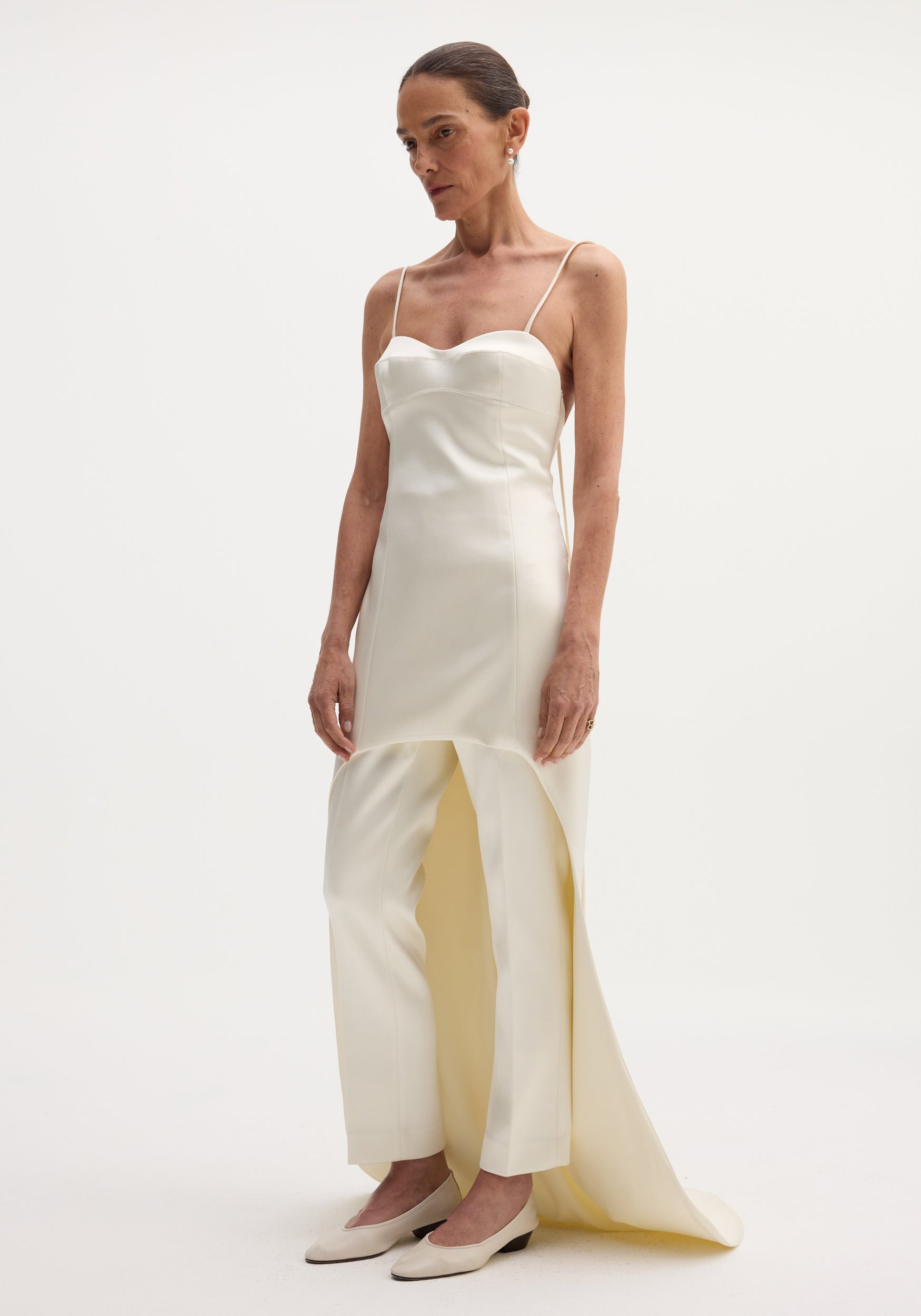 Woman wearing a Satin bustier dress with train, featuring bustier-style stitching, spaghetti straps, and an extended back hem, paired with matching straight-leg trousers.
