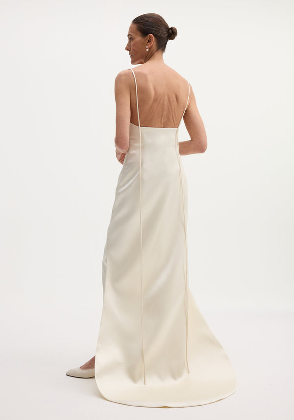 Woman in Satin bustier dress with train, wearing ivory slip dress, spaghetti straps, fitted waist, slicked-back hair, and small earrings, photographed from behind.