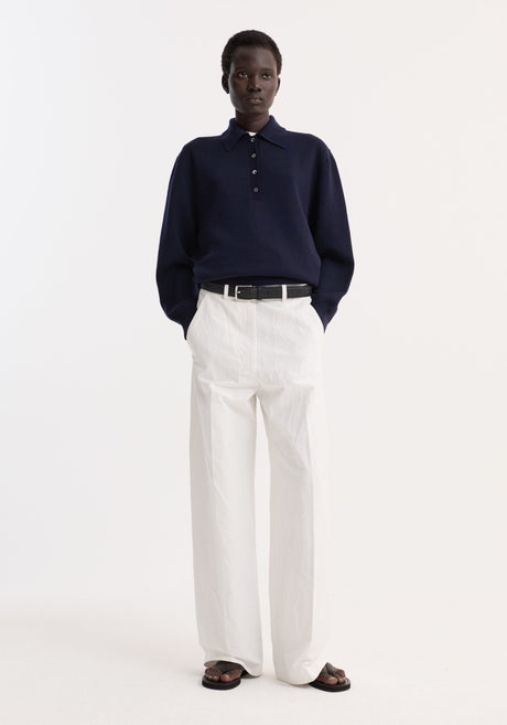 Model in Merino wool polo | navy, showcasing a structured collar and three-button placket, paired with high-waisted white trousers and black sandals.