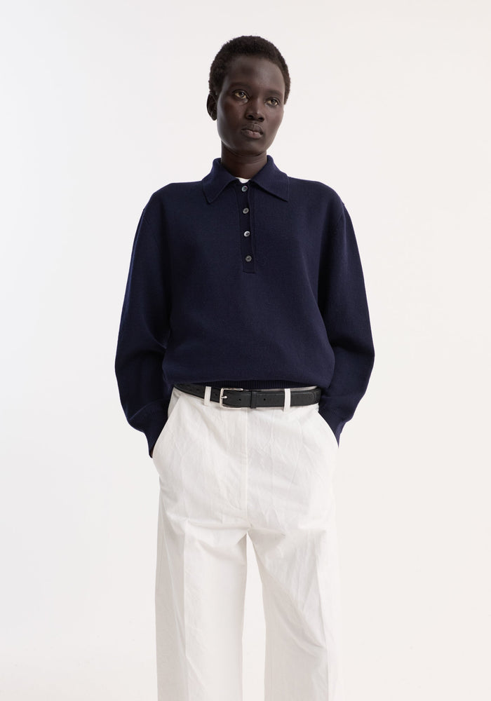 Merino wool polo in navy, worn by a person with wide-leg trousers, features a structured collar and three-button closure, made from soft merino wool.