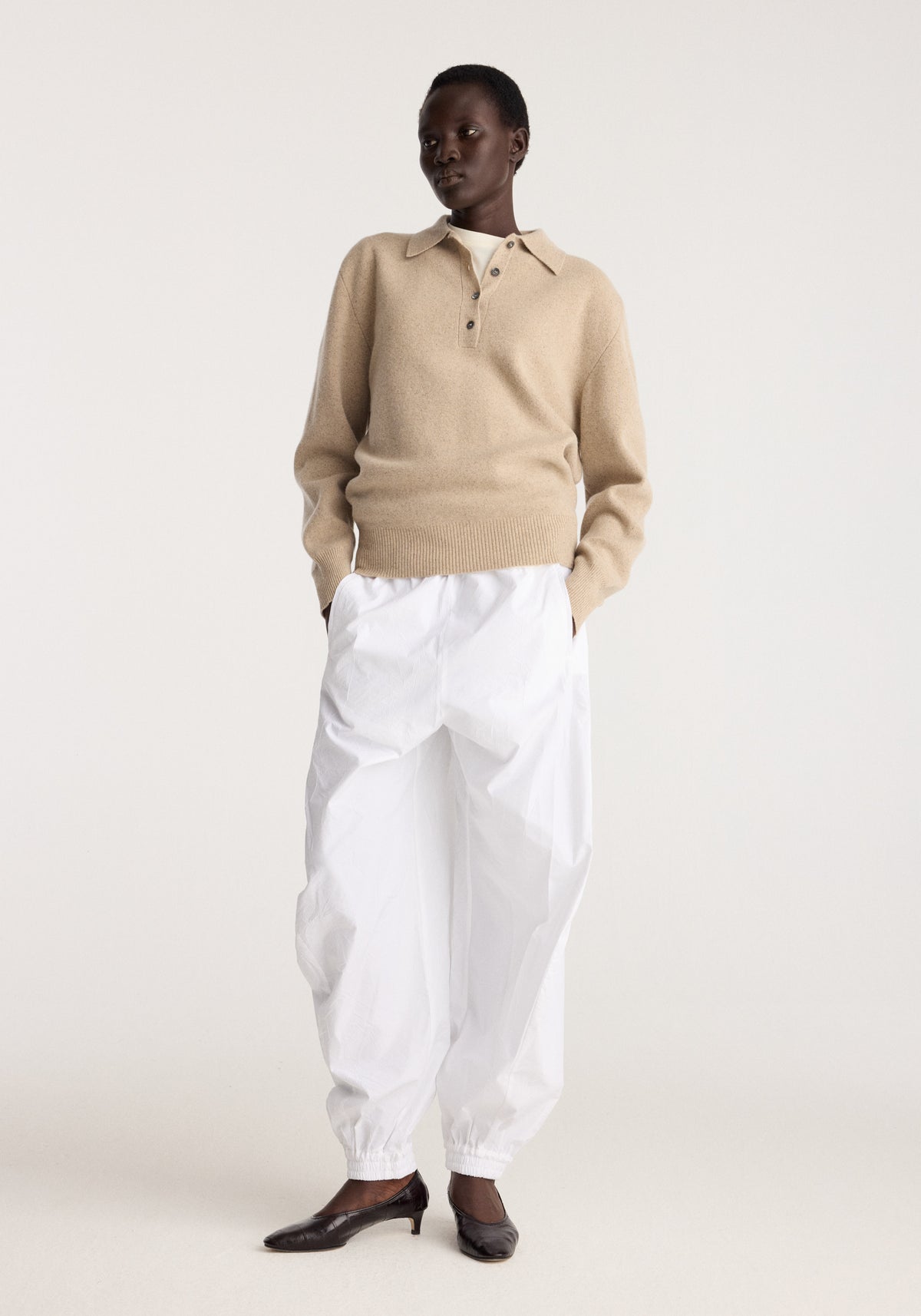 Wool cashmere polo | stone melange worn with white trousers and black leather shoes in a minimalist studio setting