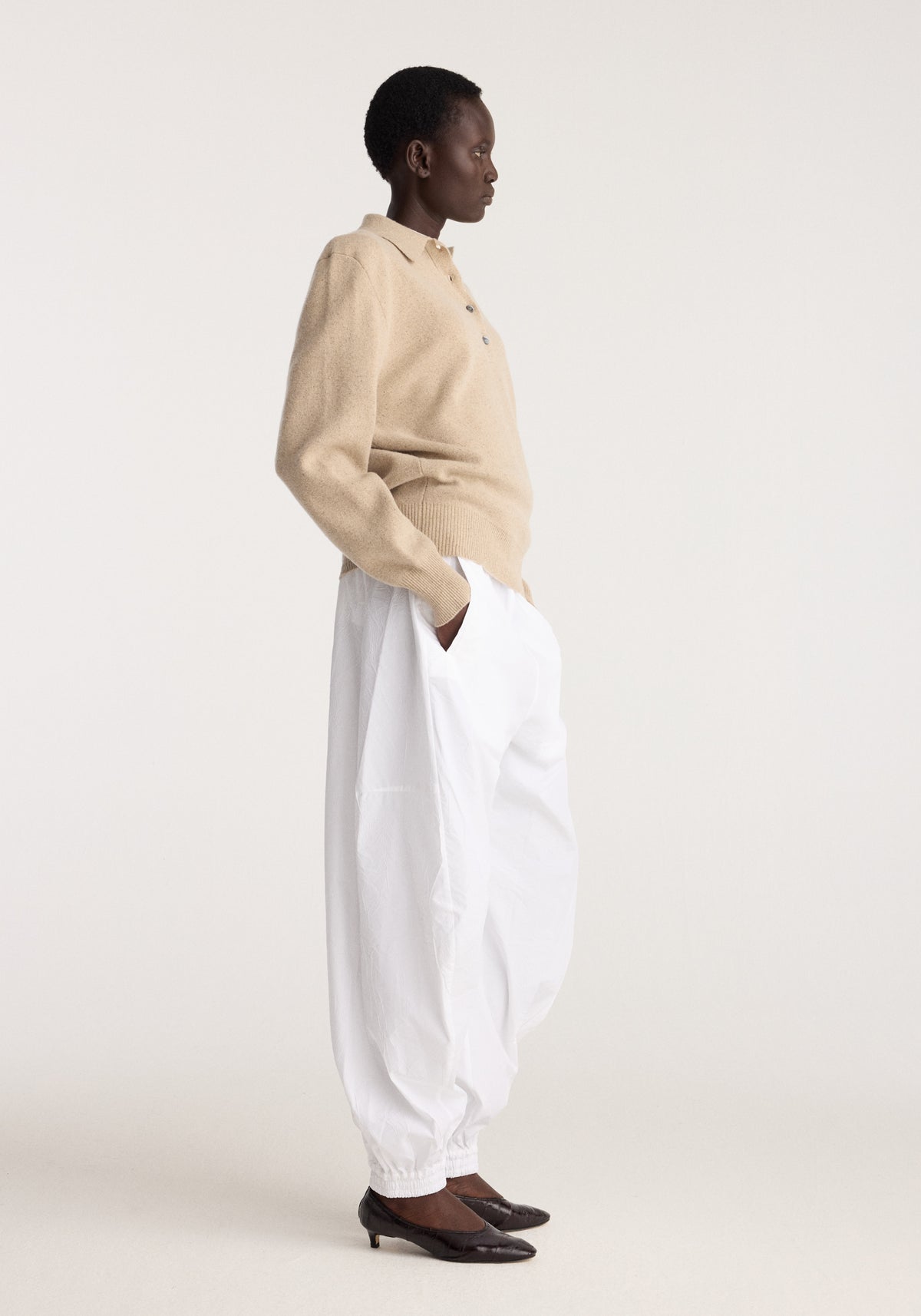 Model in side profile wearing Wool cashmere polo | stone melange with white trousers and dark loafers against a neutral studio background