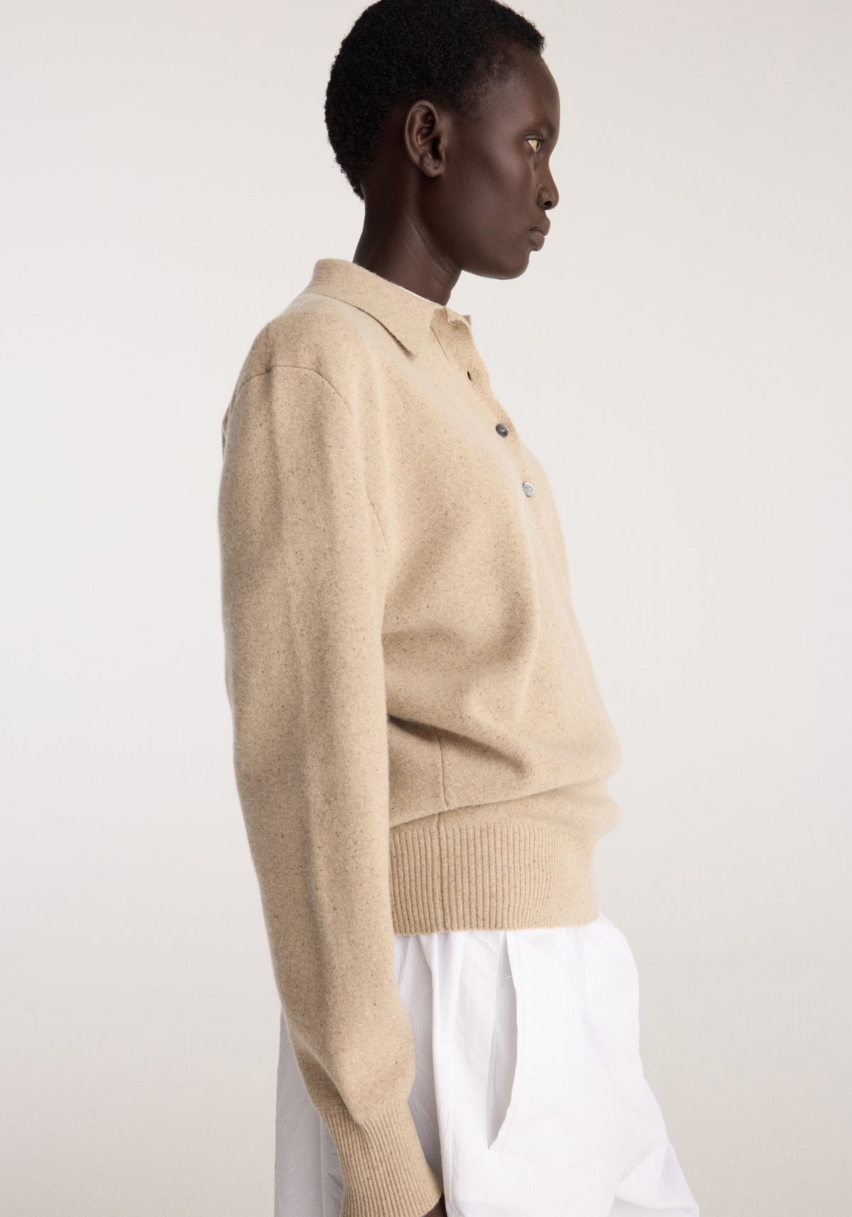 Side view of a model wearing Wool cashmere polo | stone melange with a collared neckline, button placket, long sleeves, and ribbed cuffs