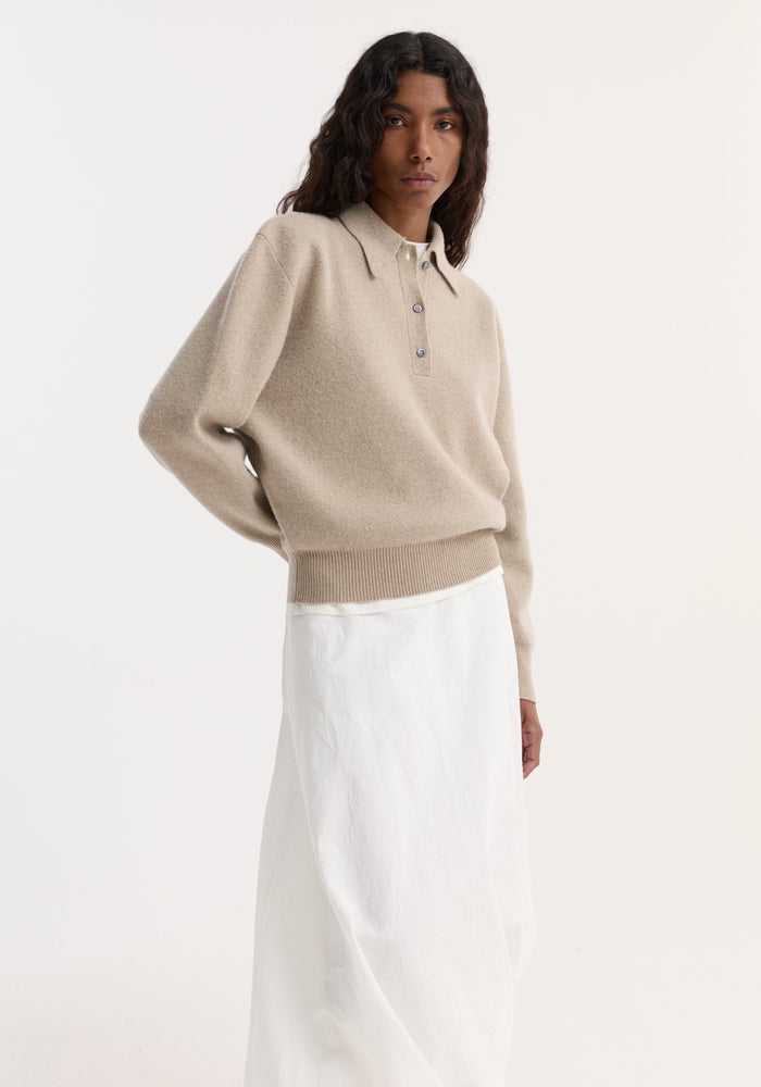Woman wearing Wool Cashmere Polo | Stone Melange with a three-button placket and structured collar, paired with a long white skirt against a plain background.