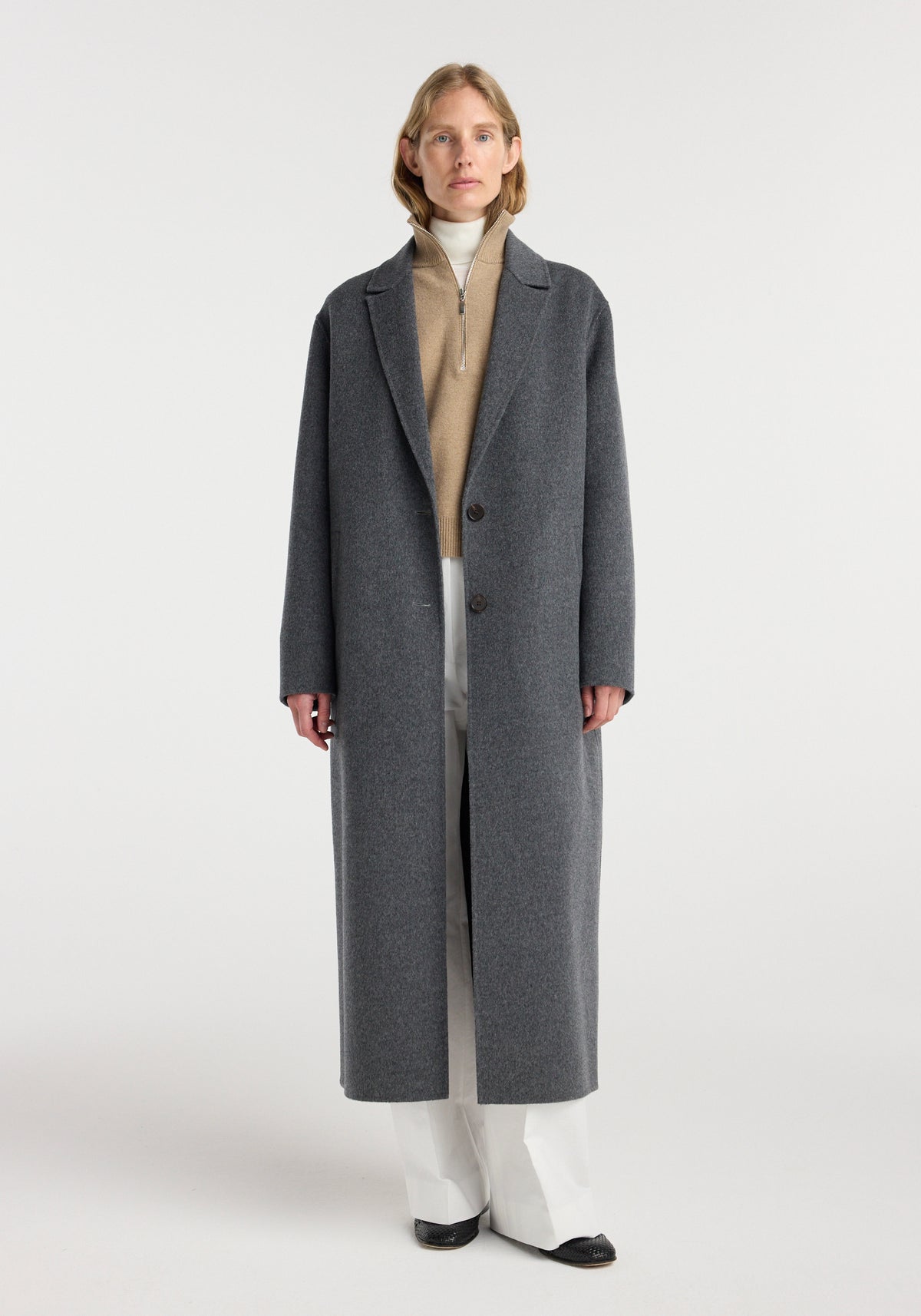 Double-faced wool long coat | dark grey melange modeled by a woman with a button front and long tailored silhouette over a cream sweater and trousers