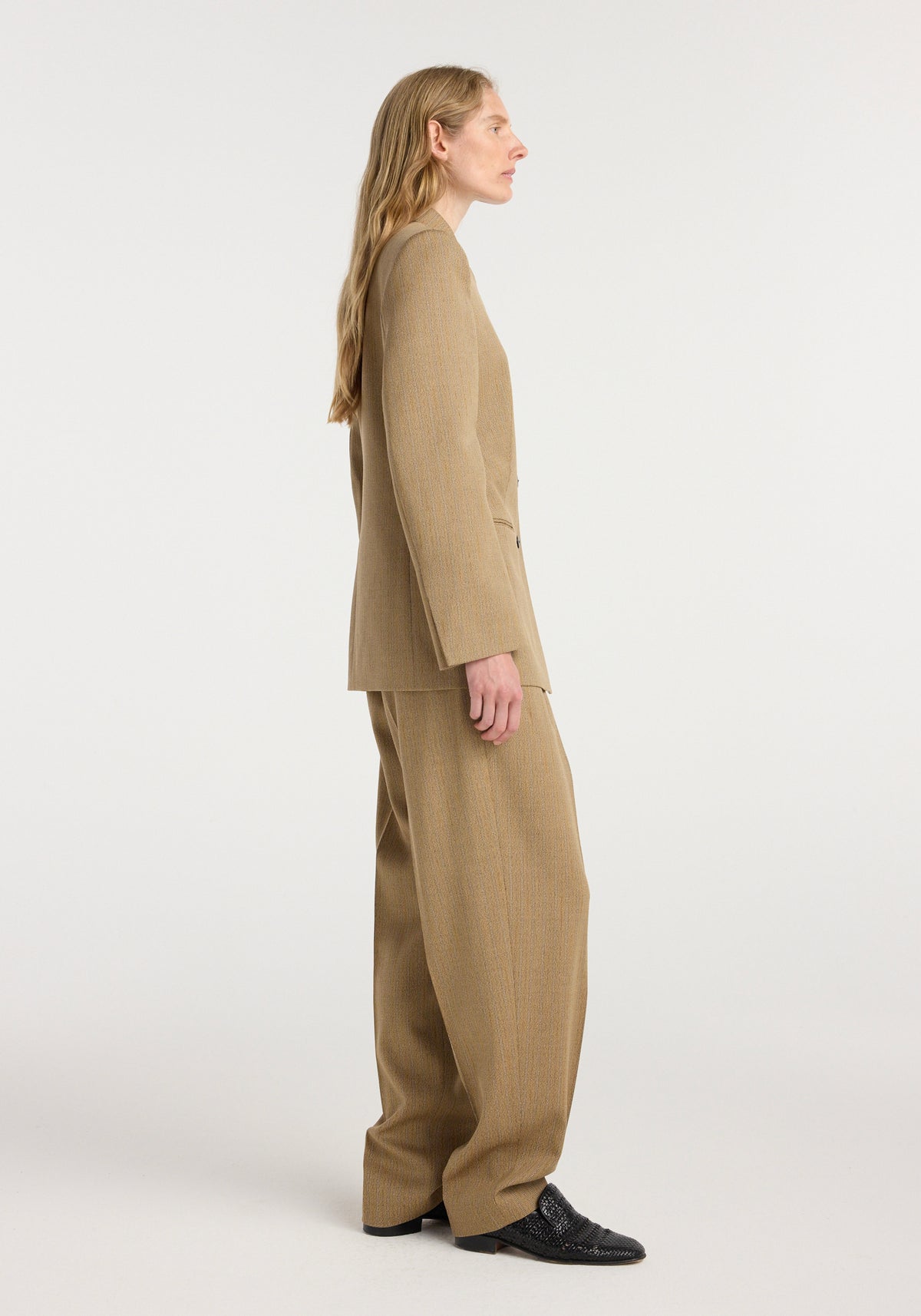 Side view of a person wearing the Overlap lapel blazer | heritage stripe in a beige stripe pattern, paired with matching wide-leg trousers and black shoes.