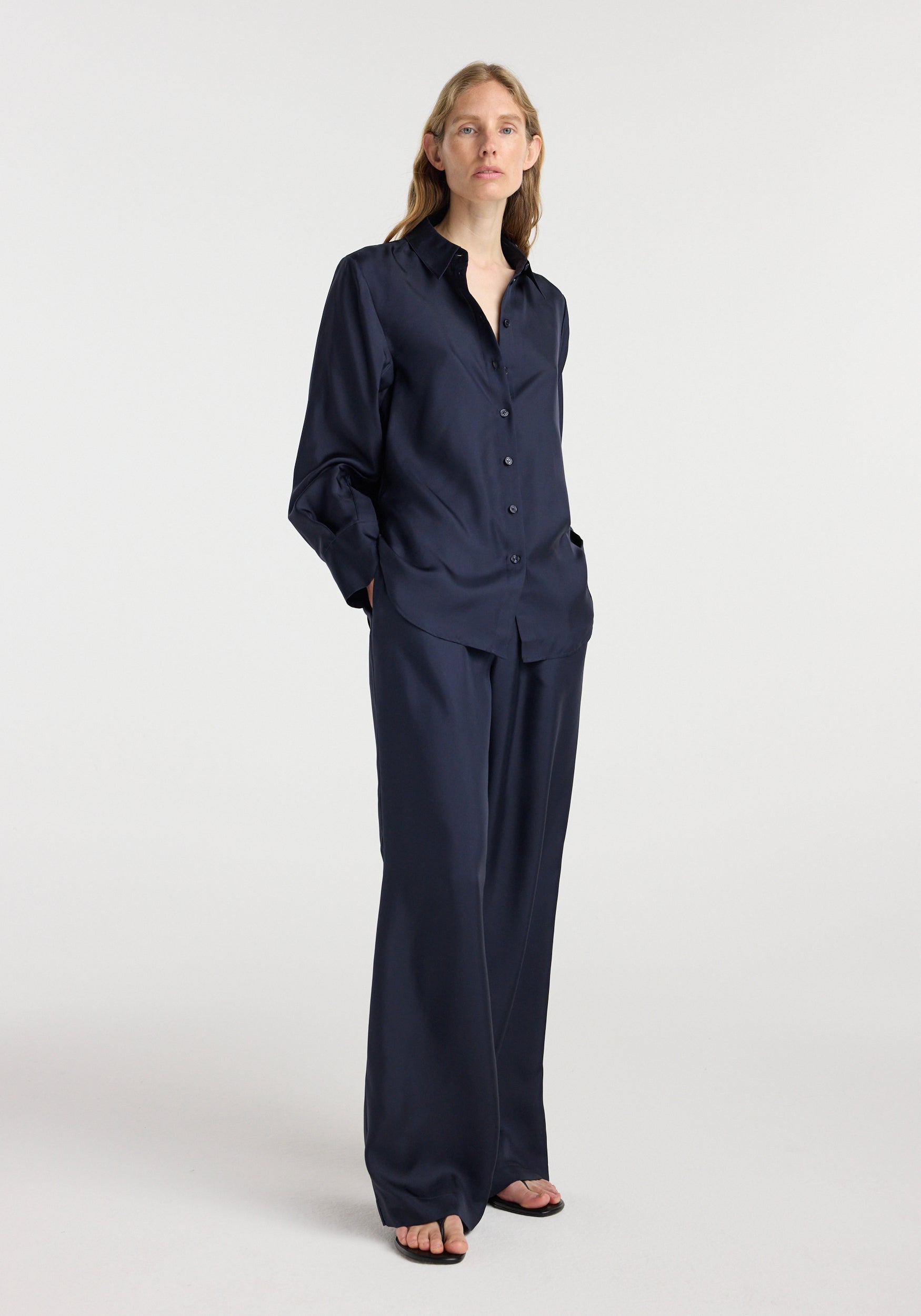 Woman wearing a dark navy silk open-sleeve detailed shirt | night paired with matching wide-leg pants in a studio setting with a neutral background.