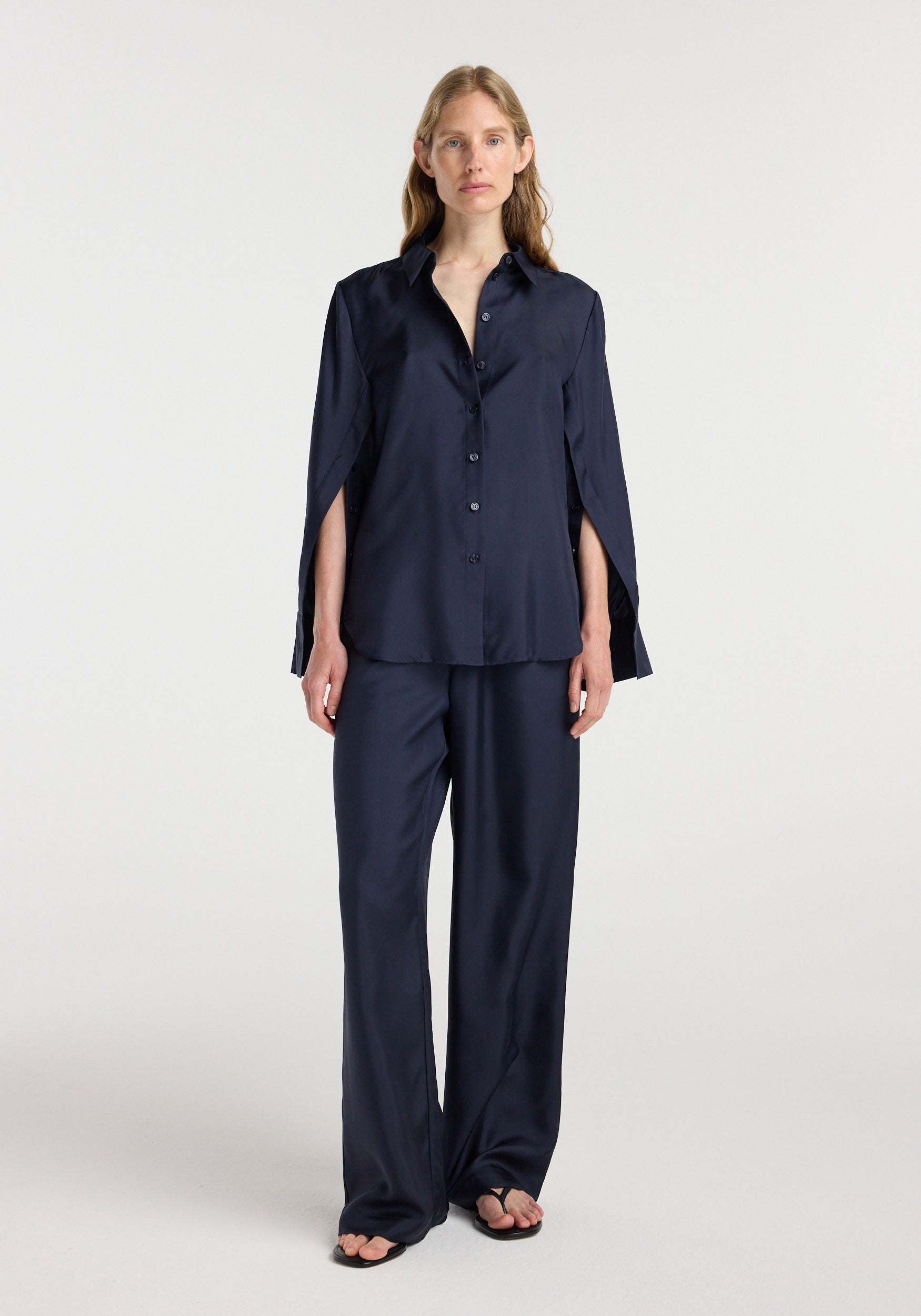 Woman wearing a navy blue Silk open-sleeve detailed shirt | night, featuring button-down front and split sleeves, paired with matching wide-leg pants and sandals.