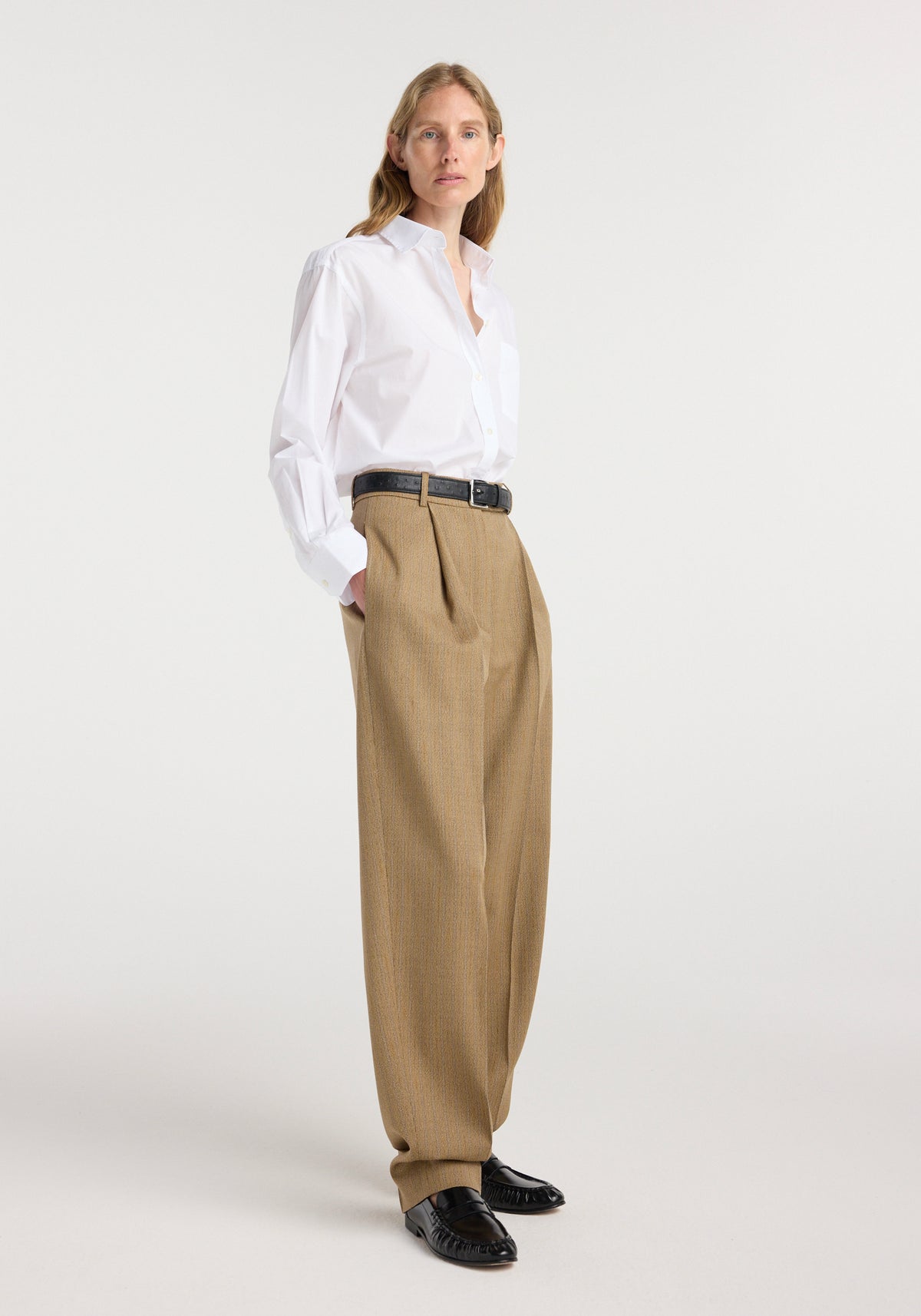 Woman wearing Classic fit shirt | optic white tucked into high-waisted beige wide-leg trousers with a black belt and black loafers, standing against a plain background.