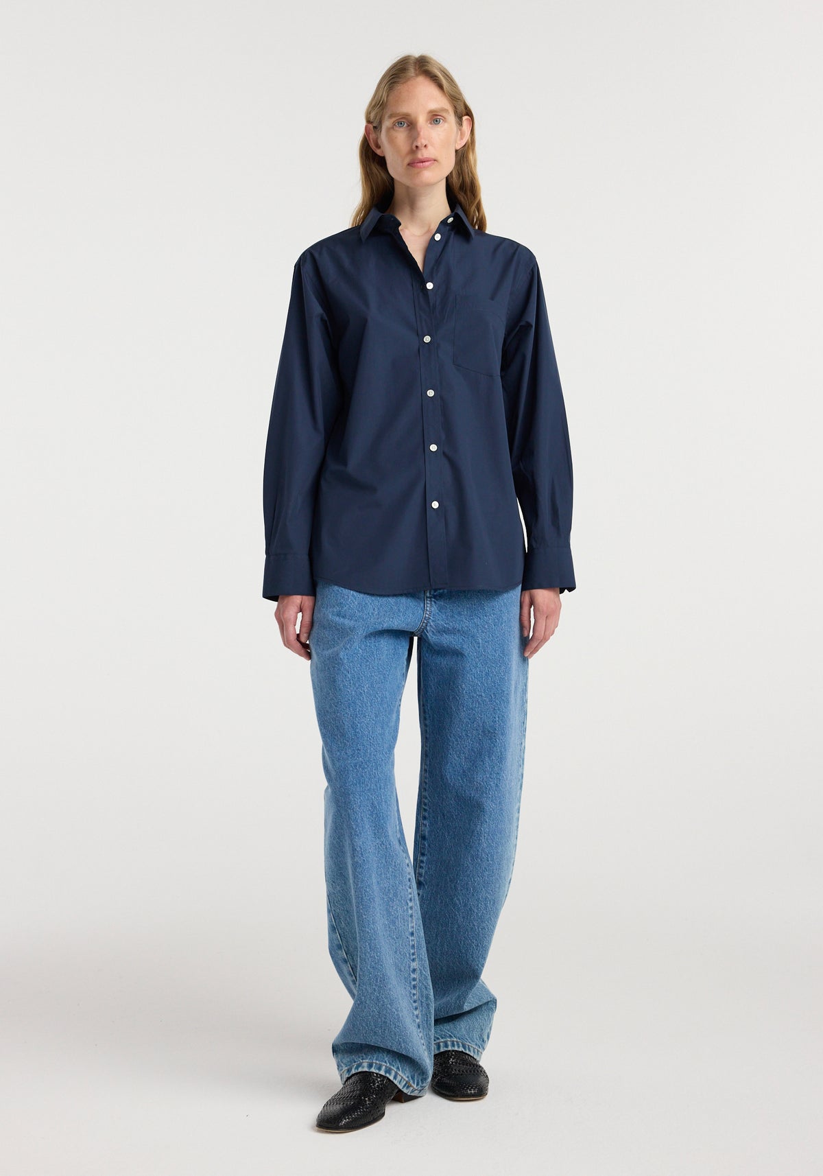 Woman wearing a navy long-sleeve button-down Classic fit shirt | navy paired with light blue wide-leg jeans and black shoes, standing against a plain white background.