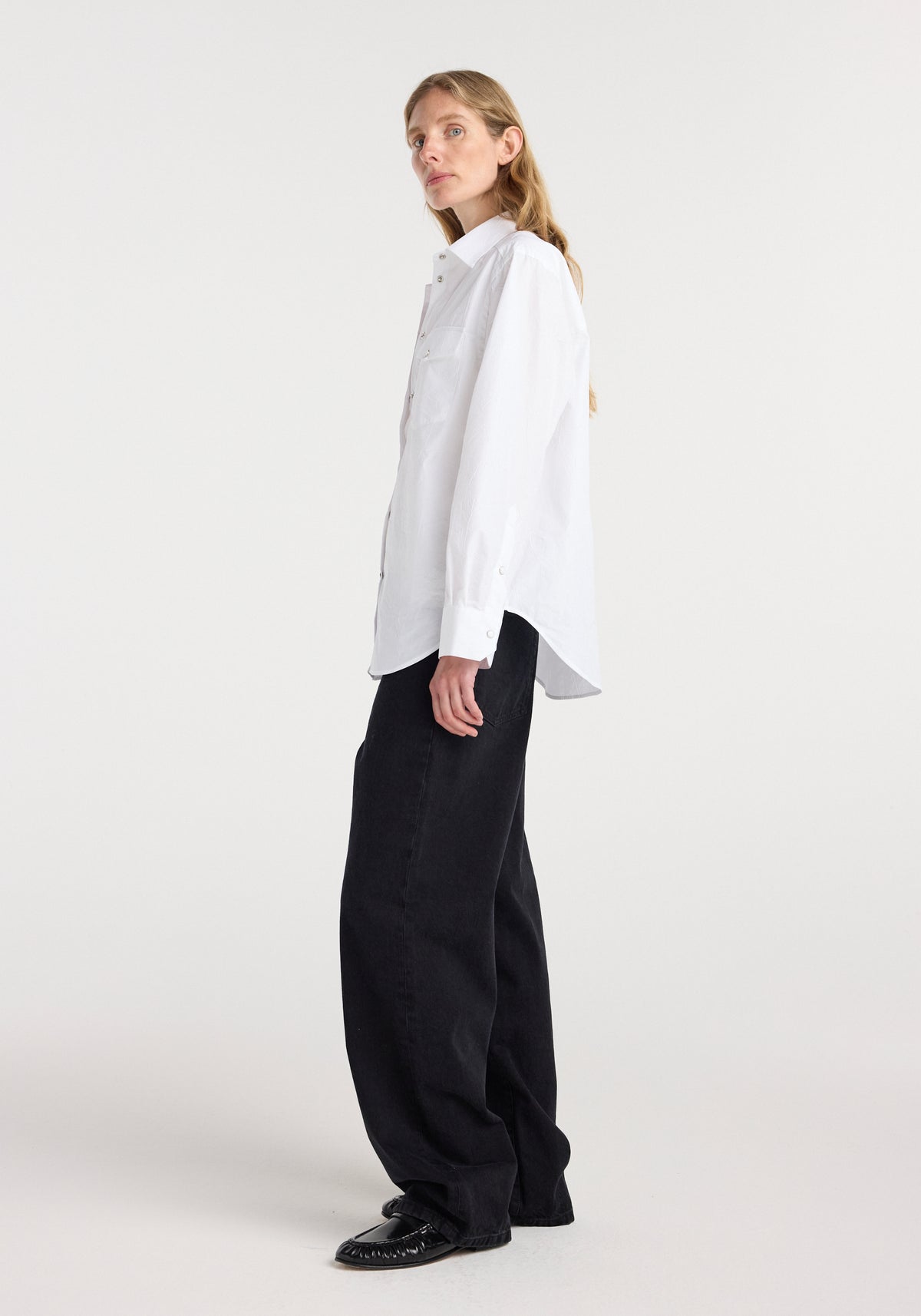 Woman wearing a crisp white Western shirt | optic white, styled with black wide-leg pants and black pointed shoes, standing against a plain background.