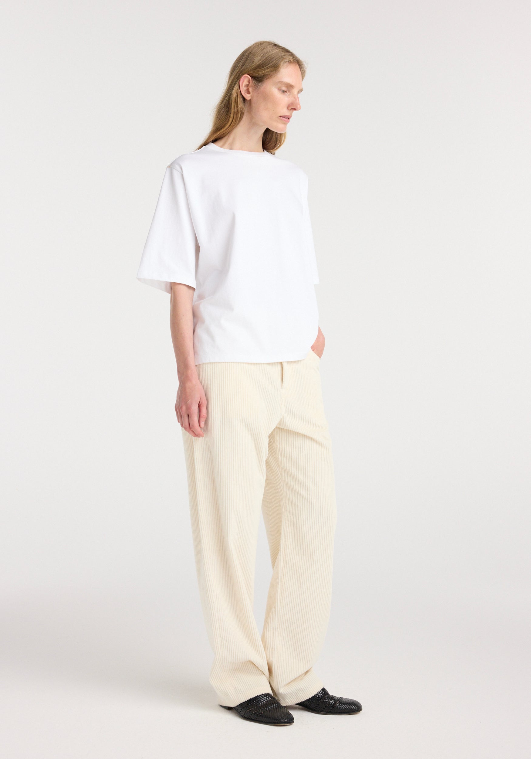 Woman wearing an oversized cotton t-shirt | optic white, paired with light beige wide-leg pants and black shoes, standing against a plain white background.