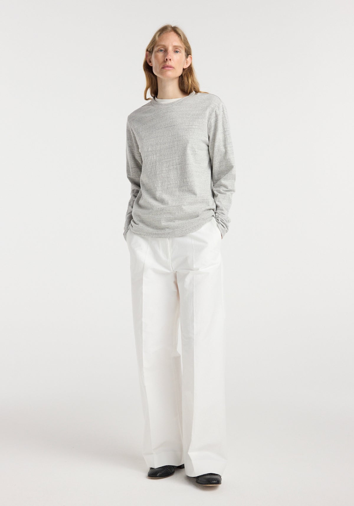 A model wearing a grey mouliné Japanese mouliné jersey long sleeve top paired with white wide-leg pants and black shoes, standing against a plain light background.
