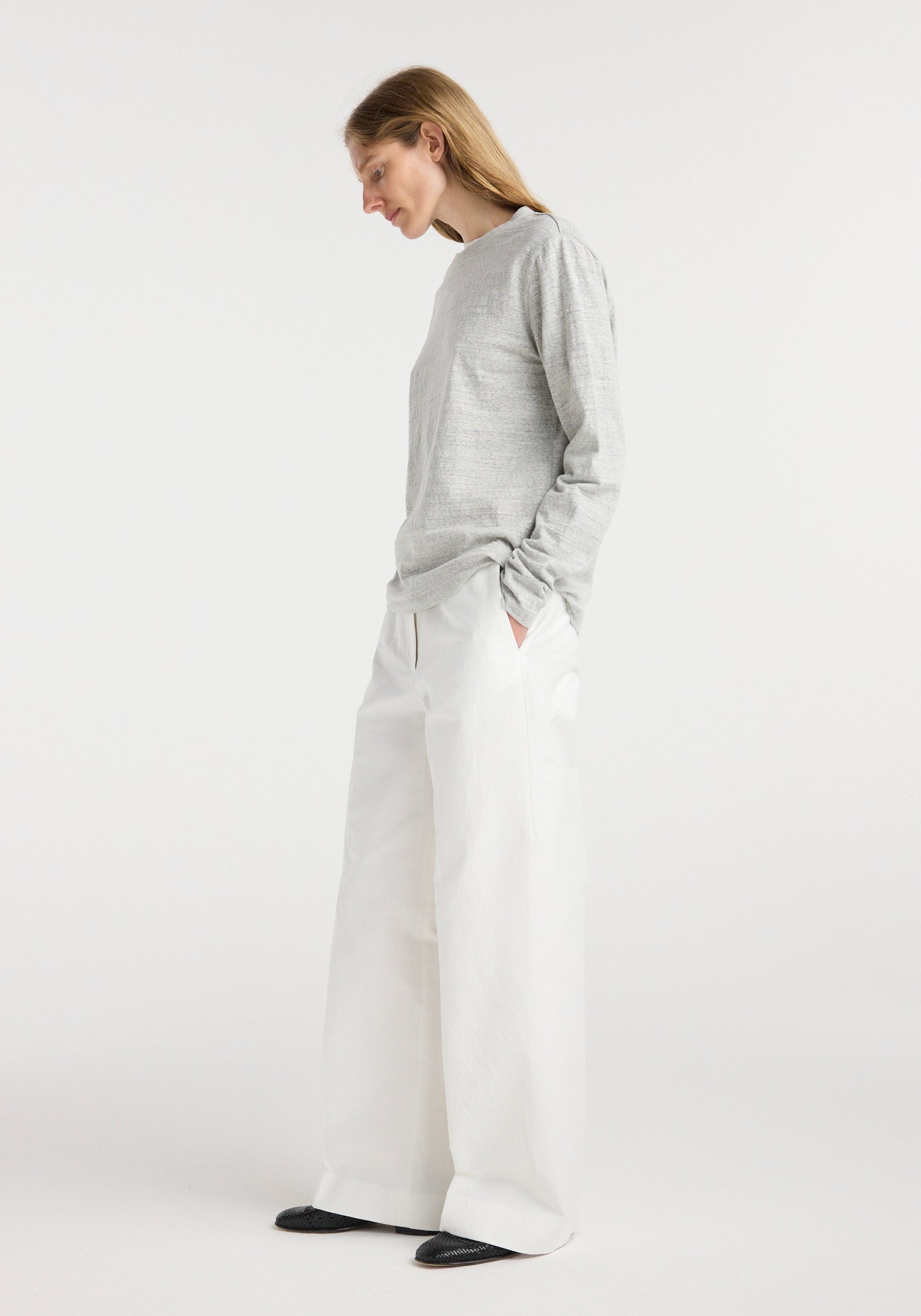 A woman wearing a grey mouliné Japanese mouliné jersey long sleeve top paired with wide-leg white trousers, standing in a relaxed pose against a plain light background.