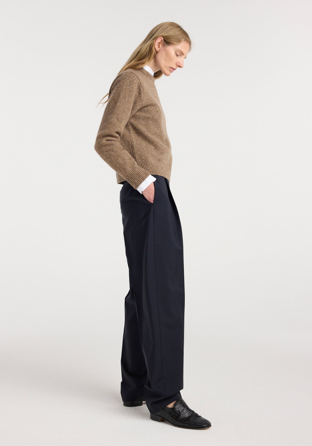 Woman wearing a fitted mouliné crewneck | mouliné taupe melange sweater with a white collared shirt underneath, paired with wide-leg black pants and black loafers against a plain background.