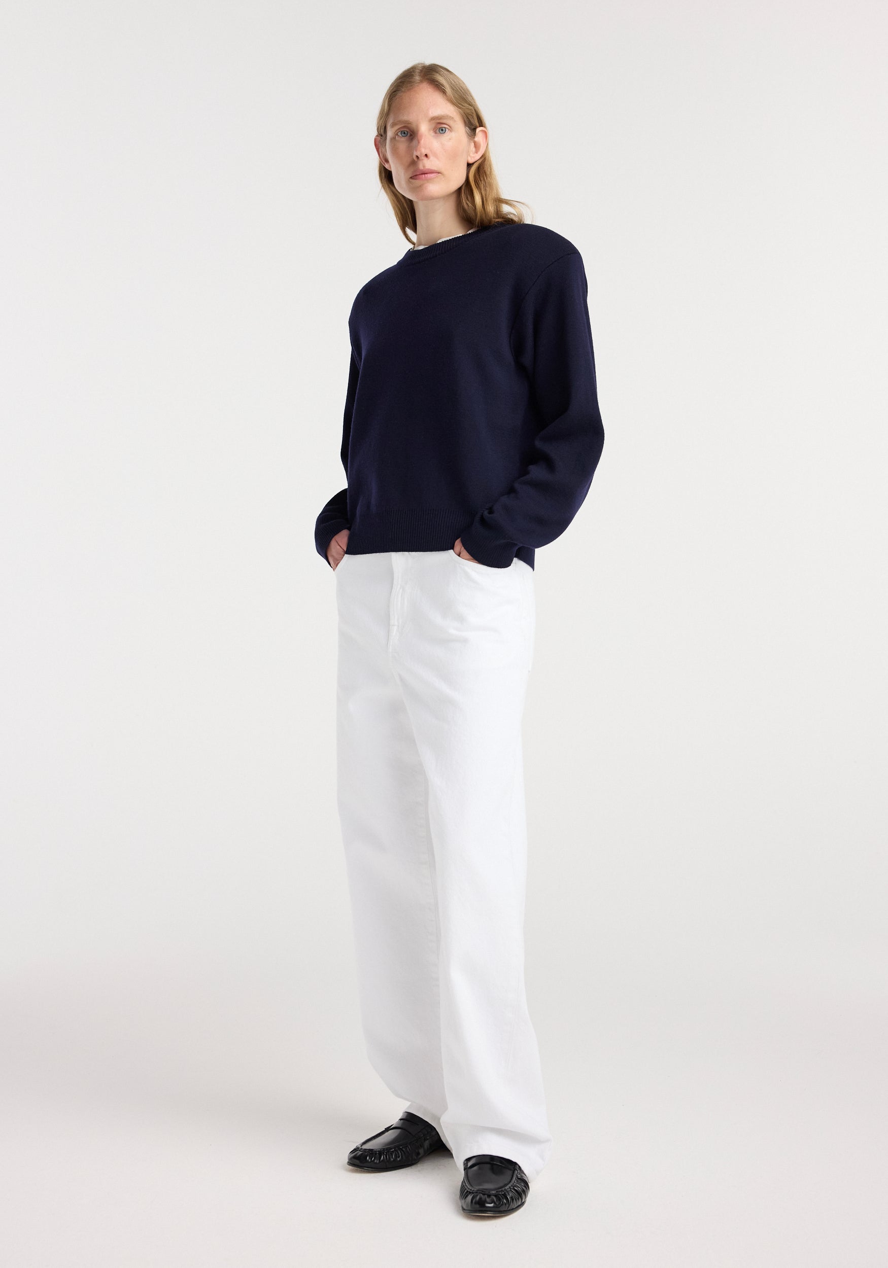 Woman wearing a navy Statement shoulder crewneck | navy with long sleeves and white wide-leg pants, standing against a plain light background